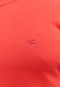 Czerwona bawełniana koszulka t-shirt z małym haftowanym logo konia w nieco ciemniejszym odcieniu. Tkanina ma gładkie, fakturowane wykończenie.