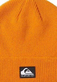 Gorro de punto naranja hecho de un tejido suave. Presenta una textura acanalada y un patch del logo de Quiksilver en negro en el pliegue. Diseño ajustado.