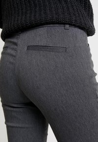 Grå figursydda byxor med texturerat tyg, utrustade med en liten bakficka och en slät yta, designade för en strömlinjeformad look.