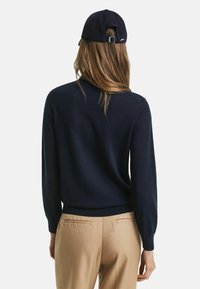 Maglione a maglia blu navy con maniche lunghe, scollo rotondo e polsini a coste. Abbinato a pantaloni beige chiaro, con dettagli posteriori minimi.