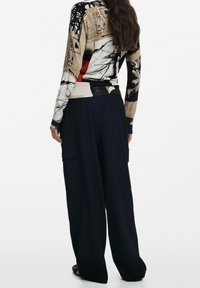 Pull en tricot avec motifs abstraits multicolores, associé à un pantalon noir ample doté de poches cargo et d'une ceinture texturée.