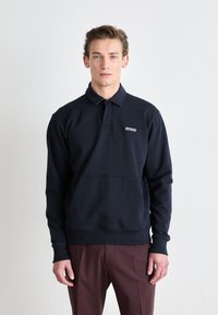 Pullover azul-marinho com gola polo e um bolso frontal. Apresenta o logótipo "BOSS" bordado e punhos e barra canelados. Corte clássico.