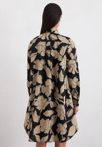 Abito camicia nero caratterizzato da ampi motivi floreali beige, maniche lunghe, polsini abbottonati e una vestibilità ampia che arriva a metà coscia.