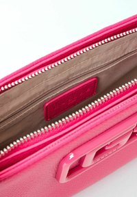 Interno della borsa in pelle rosa con una superficie liscia, chiusura con zip e un sottile tag con logo. Presenta una fodera in un marrone chiaro a contrasto e tasche.