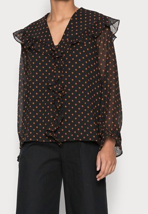 Czarna przezroczysta bluzka w pomarańczowe grochy, z falbanianym dekoltem w serek i przodem, zestawiona z czarnymi spodniami o szerokich nogawkach.