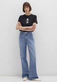 Black short-sleeve t-shirt featuring a white "Stay Spooky" graphic, paired with light blue wide-leg jeans and white sneakers.