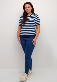 Stribet kortærmet top i lys blå og navy, parret med mørkeblå jeans og hvide sneakers. Glat tekstur og tætsiddende design.