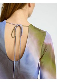 Langärmliges Oberteil mit tiefem Rückenausschnitt und einer Schleifenverschluss. Der Stoff hat einen Verlauf von blauen und grünen Farbtönen und eine glatte Textur.