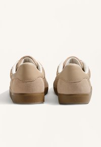 Barna velúr sportcipők fehér bőr díszítéssel, textúrált hálós panelek és gumitalpak. Alacsony profilú és kerek sarkú dizájnnal rendelkezik.