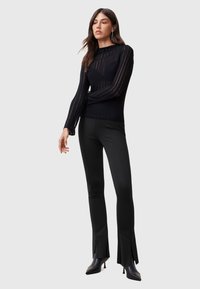 Svart långärmad topp med vertikala ränder, rundad halsringning, kombinerad med svarta slim-fit byxor med sidslitsar och spetsiga klackar.