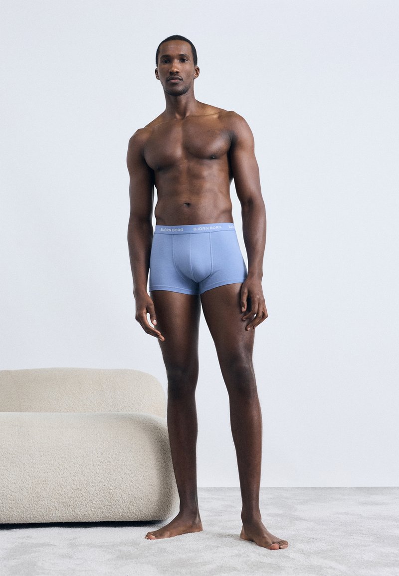 Ανοιχτό μπλε μποξεράκι με μαλακή ζώνη στη μέση που φέρει το λογότυπο "BJÖRN BORG" σε λευκό χ ρώμα. Ο μοντέλο στέκεται μπροστά από ένα ουδέτερο φόντο με απαλές υφές.