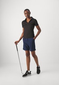 Chemise polo noire à manches courtes, short bleu marine et chaussures de sport noires. Les accessoires comprennent un club de golf. Design simple et ajusté.