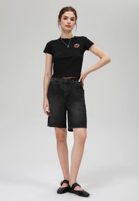 T-shirt court noir avec un graphique de soleil rouge, associé à un short en denim noir taille haute. La tenue présente un design décontracté et une texture lisse.
