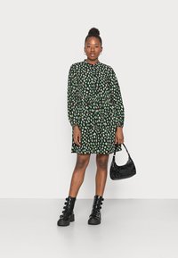 Vestido preto com padrão de folhas verdes, mangas longas, cintura franzida, combinado com uma bolsa preta de verniz e botas de combate com atacadores.