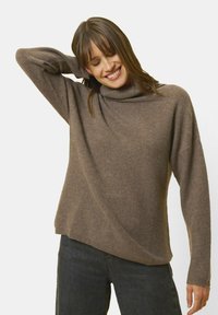 Brauner, weicher Strickpullover mit hohem Kragen und lockerer Passform. Verfügt über lange Ärmel und eine leicht A-Linienform. Getragen mit dunklen Jeans.