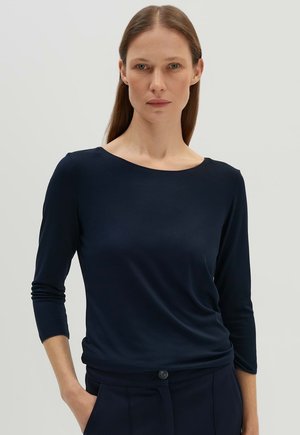 Maglia a maniche lunghe blu navy in tessuto morbido con scollatura rotonda. Vestibilità elasticizzata con sottili arricciature in vita, abbinata a pantaloni scuri.