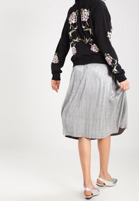 Svart sweatshirt med blommig broderi på baksidan, tillsammans med en silverfärgad plisserad midikjol och silverfärgade sandaler.