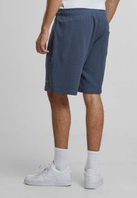 Shorts bleumarin cu un model texturat, talie elastică, buzunare laterale și o croială lejeră, asortați cu adidași albi și șosete până la gleznă.