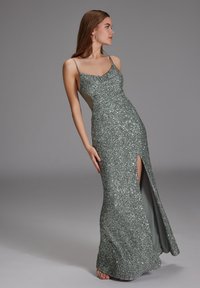 Abito da sera verde glitterato con spalline sottili, design aderente, spacco laterale e una fodera interna liscia. Tessuto con paillettes su tutta la superficie.
