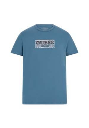 T-shirt in cotone blu con una grafica rettangolare che presenta la parola "GUESS" in lettere grasse argentate, e "EST. 1981" sotto in testo più piccolo.