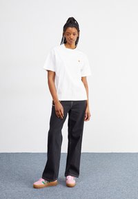 Witte katoenen t-shirt met een klein logo, gecombineerd met zwarte wijde jeans en roze platform sneakers met groene accenten.