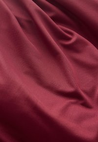 Jævn, dybrød stof med bløde folder og subtil diagonal tekstur, der skaber et flydende, elegant fald.