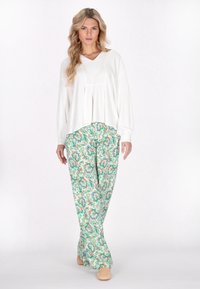 Witte langetermijn top met een V-hals en geplooide details, gecombineerd met groene losse broeken met een patroon van bloemen.