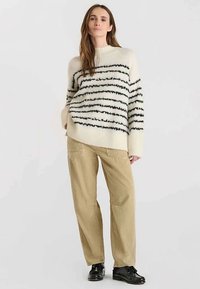 Grof gebreide trui in crème met zwarte horizontale strepen, gecombineerd met beige corduroy wijde broekspijpen en zwarte schoenen.