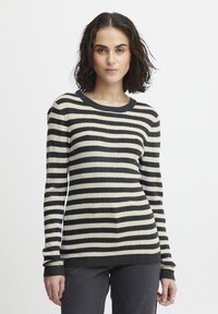 Ribbede trøje med lange ærmer, der har vandrette striber i sort og creme. Rund halsudskæring og tætsiddende design, parret med mørke jeans.
