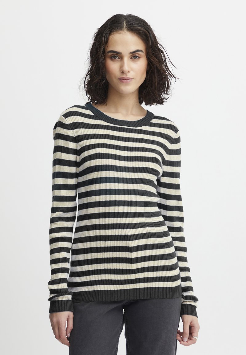 Ribbede trøje med lange ærmer, der har vandrette striber i sort og creme. Rund halsudskæring og tætsiddende design, parret med mørke jeans.