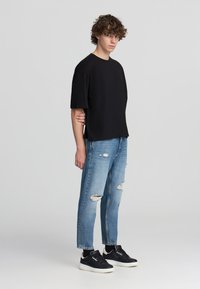 T-shirt in cotone nero, vestibilità comoda, maniche corte; abbinato a jeans blu chiaro strappati. Sneakers nere con suole bianche completano il look.