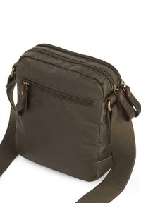 Bolso bandolera de tela marrón con tapa con cremallera, un bolsillo trasero y detalles en cuero. Cuenta con una correa de tela ajustable y detalles de costura.