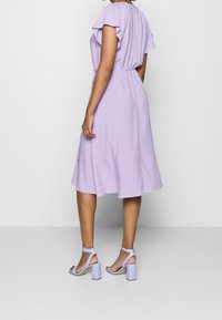 Svetle fialové šaty s volánkovými rukávy, se staženým pasem a splývavou sukní. V kombinaci s levandulovými sandály na blokovém podpatku.