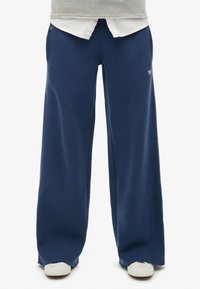 Navyblauwe wijdvallende sweatpants van zachte stof. Heeft zijzakken en een klein logo aan de voorkant. Minimalistisch ontwerp met een relaxte pasvorm.
