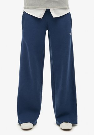 Pantaloni della tuta a gamba larga blu navy realizzati in tessuto morbido. Caratterizzati da tasche laterali e un piccolo logo sulla parte frontale. Design minimalista con una vestibilità comoda.