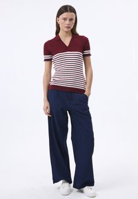 Polo en tricot à manches courtes rayé rouge et blanc avec un tissu texturé, associé à un pantalon ample bleu marine et des baskets blanches.