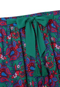 Kleurrijke stof met bloemenpatroon, met een groene tailleband en een gestrikte strik en kwastjes in bijpassend groen.