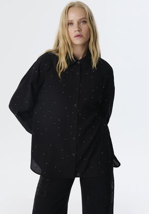 Zwarte button-up shirt met een gestructureerd patroon, voorzien van witte decoratieve stippen. Lange mouwen en een relaxte pasvorm.