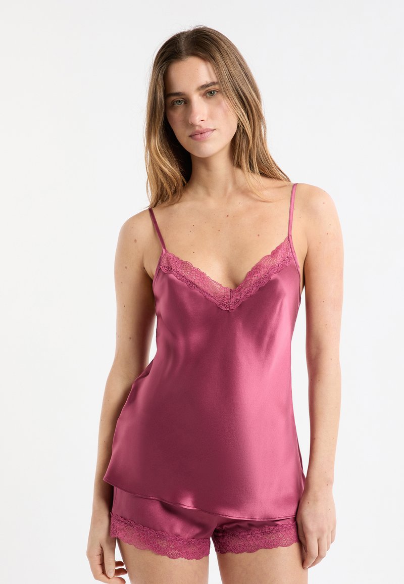 Komplet z satynowej koszulki na cienkich ramiączkach i szortów w głębokim różowym kolorze z delikatną koronką wzdłuż dekoltu i brzegu. Regulowane ramiączka umożliwiają dopasowanie do sylwetki.