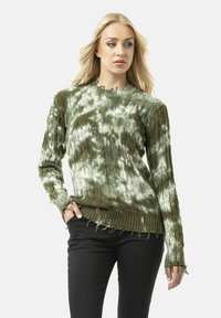 Grüner Kabelstrickpullover mit einem Batikmuster. Mit geripptem Saum und ausgefransten Kanten. Lange Ärmel mit strukturierter Oberflächenbeschaffenheit.