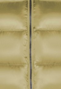 Chaqueta tipo abrigo en tejido brillante de color amarillo claro, con secciones acolchadas verticales y una cremallera metálica central. Textura suave, diseño minimalista.