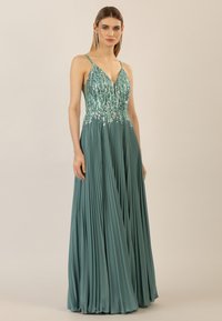 Un abito plissettato color teal con scollatura a V, corpo decorato e spalline sottili. Il tessuto ha una texture liscia con un effetto luminoso.