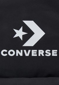 Fondo de tela negra con el texto blanco "Converse", una estrella y un logo de flecha, con una superficie texturizada y un diseño gráfico audaz.