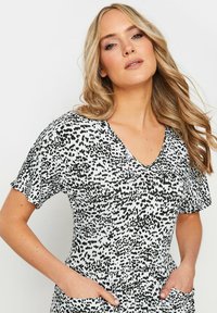 Schwarzes und weißes kurzärmliges Kleid mit V-Ausschnitt, das ein gesprenkeltes Muster, weichen Stoff und Seitentaschen aufweist.