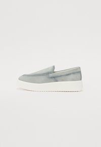 Chaussures à enfiler en daim gris clair avec une semelle en caoutchouc blanche. Présentent un design minimaliste et des détails cousus le long du devant.