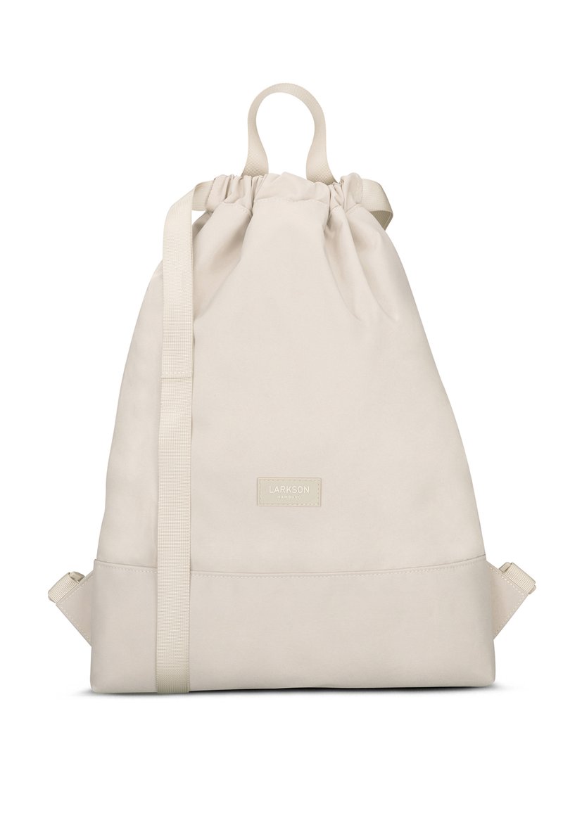 Sac à dos à cordon beige en tissu doux, doté d'une poignée supérieure, de bretelles réglables et d'une base rectangulaire avec un écusson logo.