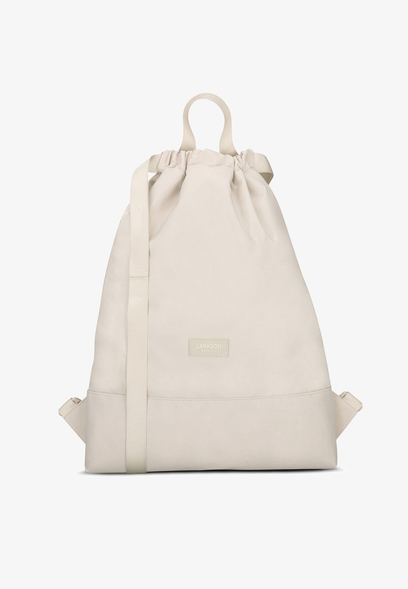 Beige-nauha-reppu pehmeästä kankaasta, jossa on ylhäällä kantokahva, säädettävät olkaimet ja suorakulmainen pohja, jossa on logopatch.