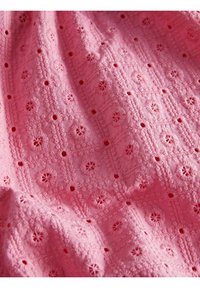 Rožinė siuvinėta medžiaga, kurioje pavaizduoti gėlių raštai su mažais išpjovimais, tekstūruota paviršius ir sudėtingas siuvinėjimas deimantų tinklelio raštu.