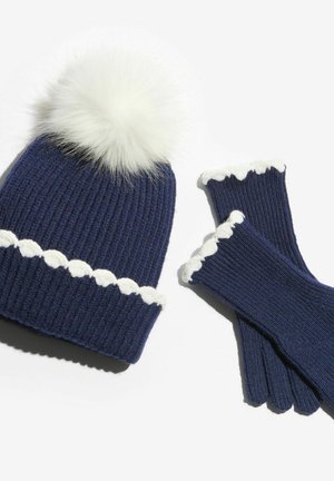 Berretto a coste blu navy con pompon in pelliccia bianca e guanti abbinati con bordo smerlato bianco ai polsini.