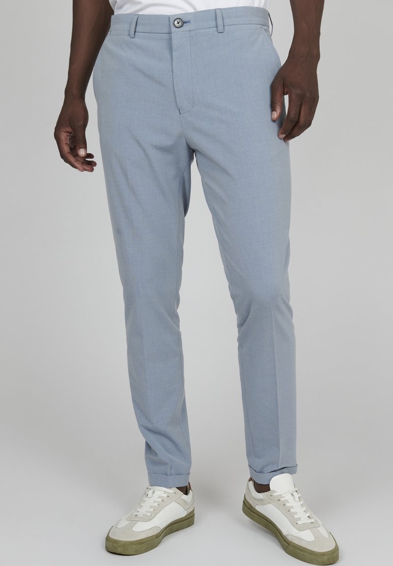 Jasnoniebieskie spersonalizowane spodnie z fakturowanej tkaniny, z zapięciem na guzik, dopasowany krój i mankiety na nogawkach, zestawione z białymi trampkami.